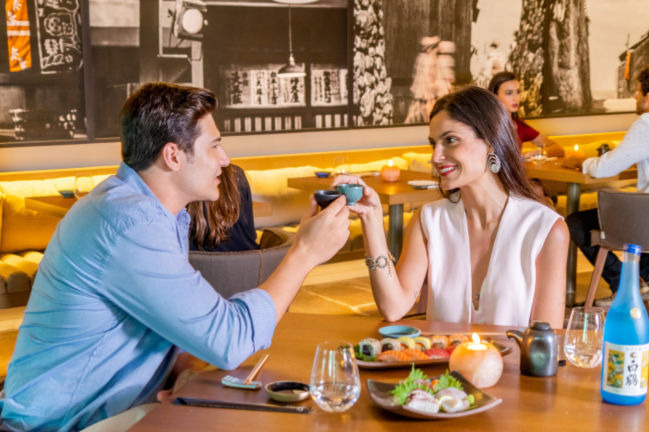 Homem e mulher em um encontro romântico em um restaurante, compartilhando uma refeição e brindando no restaurante Shiso Grand Hyatt