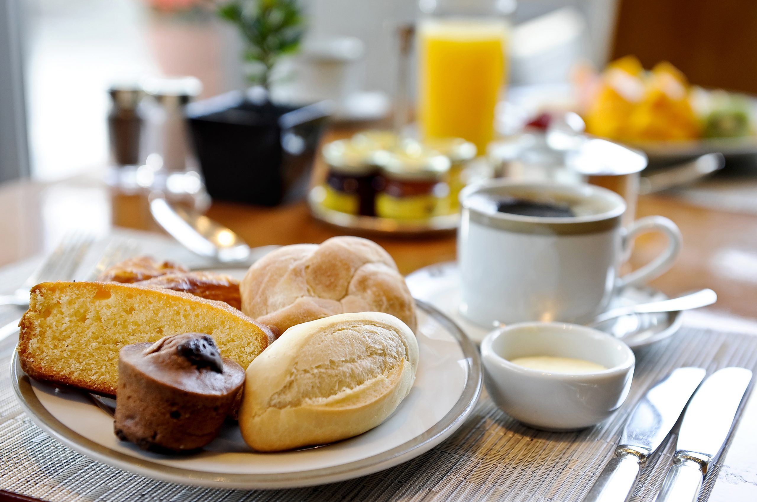 mesa de café da manhã com prato cheio de pães diferentes e uma xícara de café ao lado