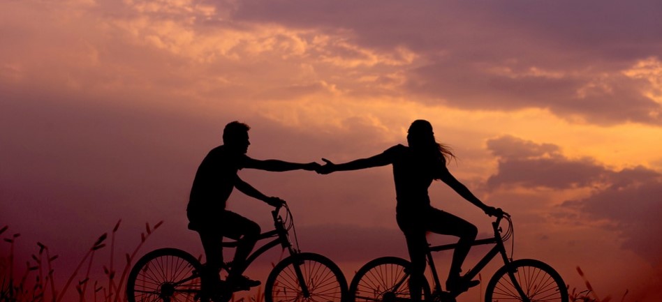 casal andando de bicicleta e dando as mãos