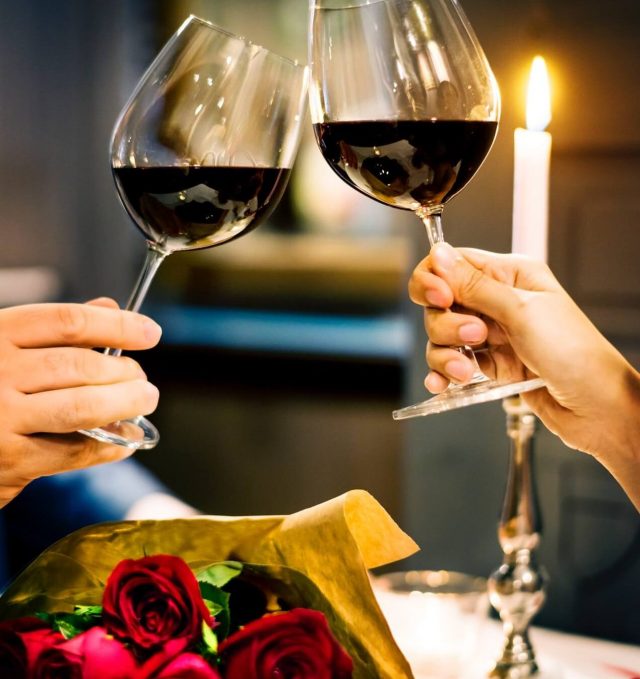 Casal brindando com taça de vinho com rosas sobre a mesa