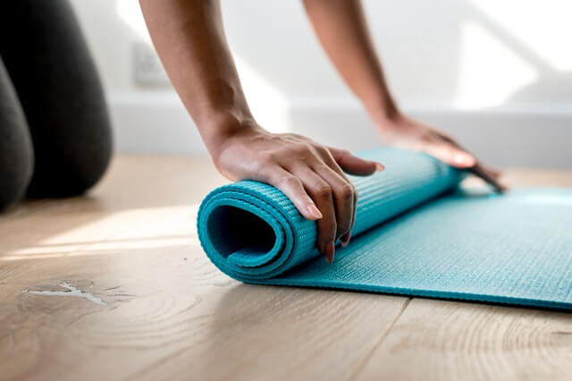 A imagem mostra uma pessoa enrolando um tapete de yoga