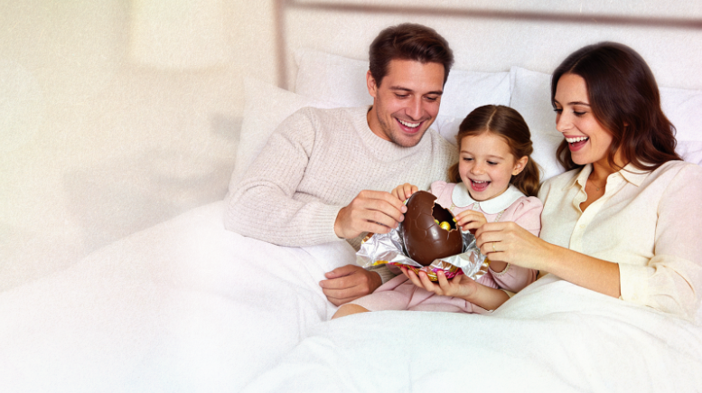 Família alegre na cama abrindo um ovo de páscoa.