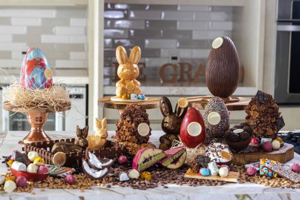 Mesa com variedade de ovos de chocolate artesanais e esculturas de coelho para a Páscoa e decorados com confeitos coloridos.