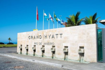 Entrada do Grand Hyatt Rio de Janeiro com letreiro na fachada, bandeiras ao alto, palmeiras e céu azul.